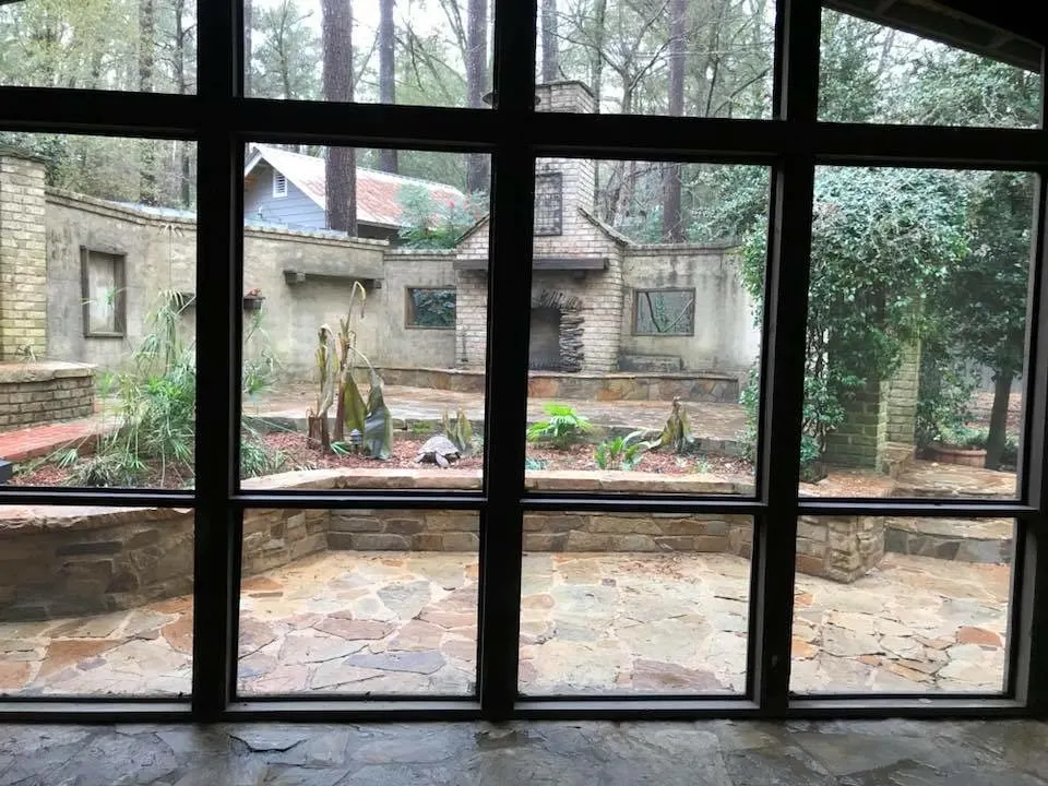 View out through the black-framed window walls of a three-season room to a stone patio